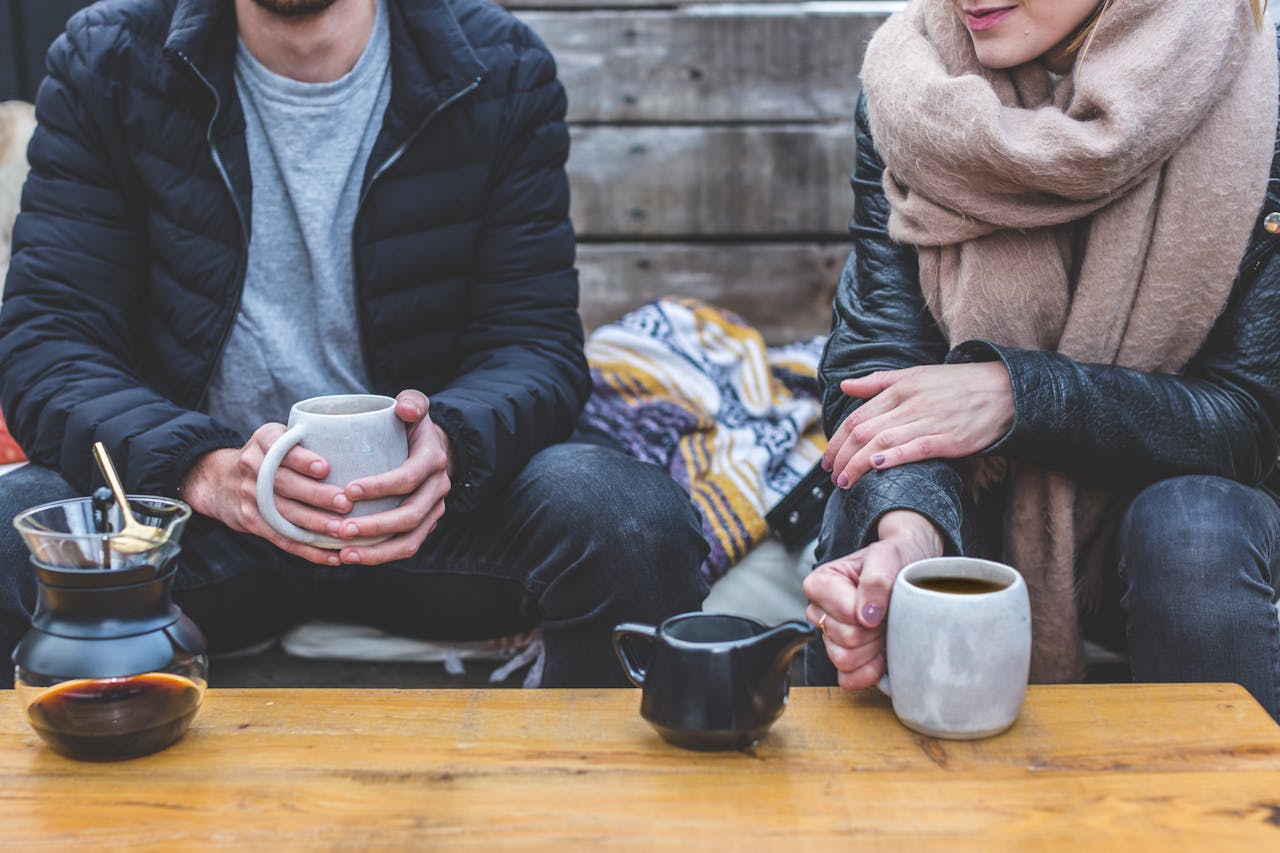 Two adults enjoying a cozy coffee break outdoors, wrapped in warm clothing.