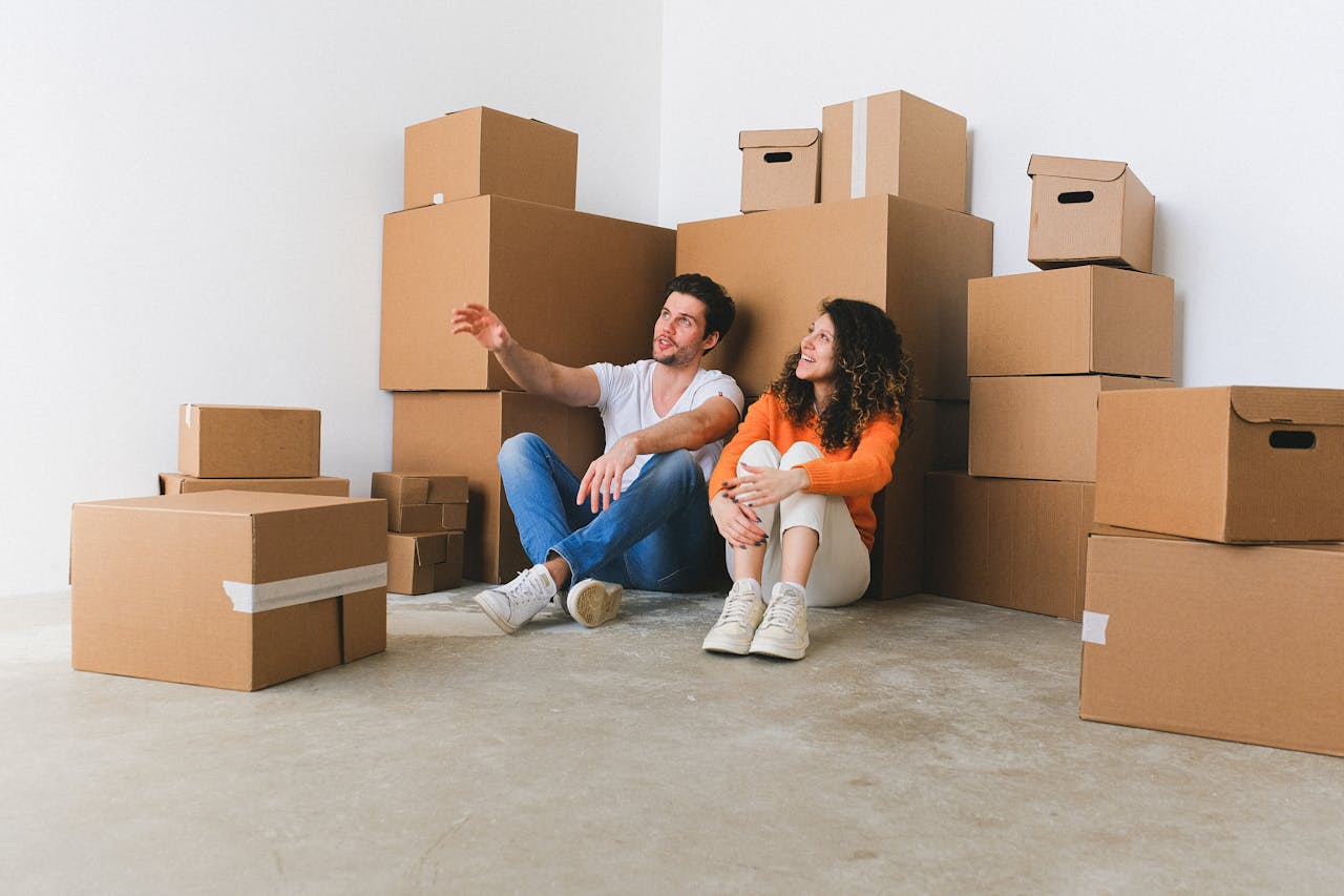 Young couple sitting among cardboard boxes in their new home, taking a break from moving.